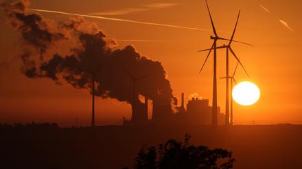 Die Sonne geht über dem Braunkohle-Tagebau Garzweiler auf, während Dampf aus dem Braunkohle-Kraftwerk Neurath des Energiekonzerns RWE aufsteigt und RWE-Windräder sich drehen. 