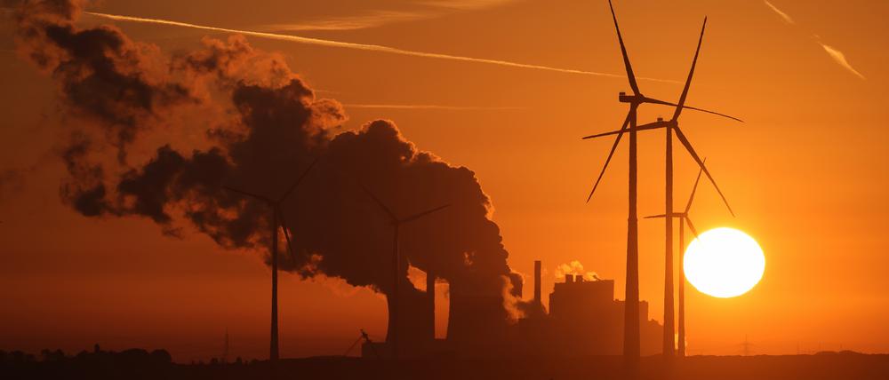 Die Sonne geht über dem Braunkohle-Tagebau Garzweiler auf, während Dampf aus dem Braunkohle-Kraftwerk Neurath des Energiekonzerns RWE aufsteigt und RWE-Windräder sich drehen.
