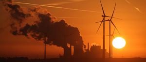 Die Sonne geht über dem Braunkohle-Tagebau Garzweiler auf, während Dampf aus dem Braunkohle-Kraftwerk Neurath des Energiekonzerns RWE aufsteigt und RWE-Windräder sich drehen.
