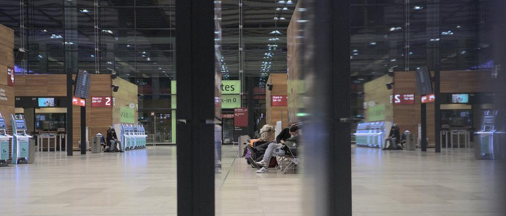 Einige wenige Fluggäste sitzen am frühen Morgen in der Halle des Flughafens BER. Die Gewerkschaft Verdi hat das Bodenpersonal der Lufthansa zu einem ganztägigen Warnstreik an mehreren Flughäfen am Mittwoch aufgerufen.