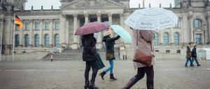 Touristen halten bei nasskaltem Wetter Regenschirme in den Händen und gehen am Reichstagsgebäude vorbei.