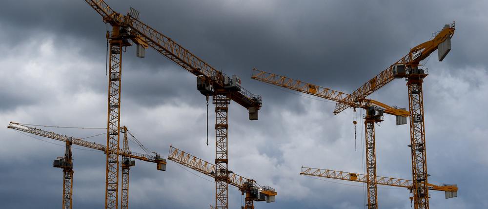 Kräne einer Baustelle sind vor dunklen Wolken zu sehen.