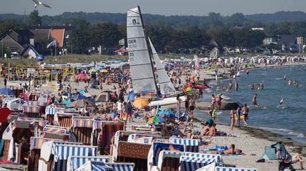 Passantinnen und Passanten genießen das Sonnenwetter am Strand der Ostsee.