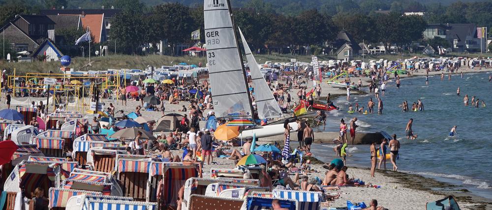 Passantinnen und Passanten genießen das Sonnenwetter am Strand der Ostsee.