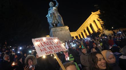 Menschen stehen bei einer Demonstration unter dem Motto «Lichtermeer für Demokratie, gegen Rassismus, Antisemitismus und Hetze» mit einem Plakat unterhalb der Ruhmeshalle und der Bavaria auf der Theresienwiese.