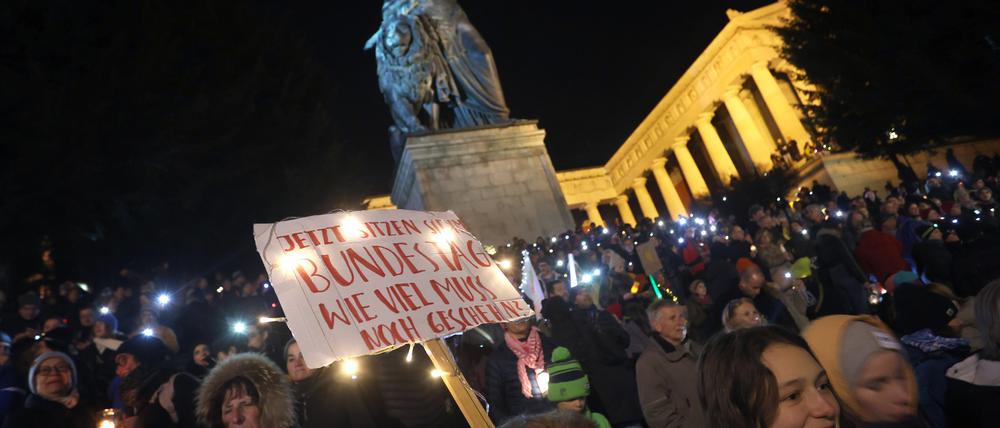 Menschen stehen bei einer Demonstration unter dem Motto «Lichtermeer für Demokratie, gegen Rassismus, Antisemitismus und Hetze» mit einem Plakat unterhalb der Ruhmeshalle und der Bavaria auf der Theresienwiese.