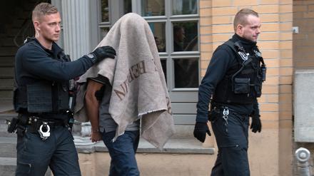 Polizisten führen einen verdächtigen Mann nach einer Razzia ab.