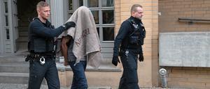 Polizisten führen einen verdächtigen Mann nach einer Razzia ab.