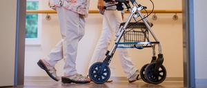 Eine Pflegekraft geht in einem Pflegeheim mit einer älteren Dame mit Rollator über einen Korridor. (Symbolbild)