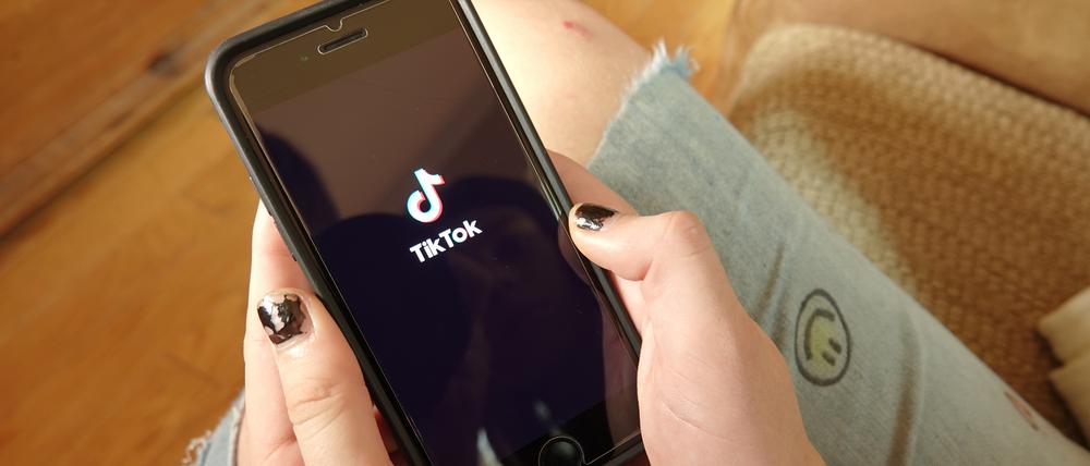 Ein Mädchen hält ein Handy mit der App von Tiktok in der Hand.