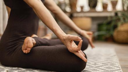 Eine Frau sitzt im Lotussitz auf einer Yogamatte.