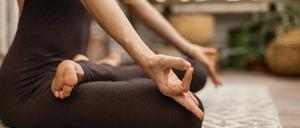 Eine Frau sitzt im Lotussitz auf einer Yogamatte.