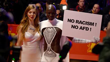 15.02.2024, Berlin: Papis Loveday (r) steht am Eröffnungsabend der Berlinale mit einem Protestschild "No Racism ! No AFD !" neben Schauspielerin Pheline Roggan auf dem Roten Teppich. Es wird der Film "Small Things Like These" gezeigt. Die 74. Internationalen Filmfestspiele Berlin finden vom 15. - 25.02.2024 statt. Foto: Monika Skolimowska/dpa +++ dpa-Bildfunk +++