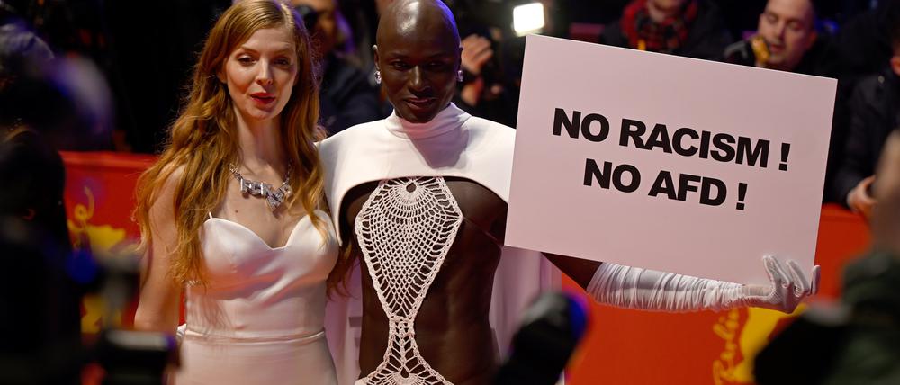15.02.2024, Berlin: Papis Loveday (r) steht am Eröffnungsabend der Berlinale mit einem Protestschild "No Racism ! No AFD !" neben Schauspielerin Pheline Roggan auf dem Roten Teppich. Es wird der Film "Small Things Like These" gezeigt. Die 74. Internationalen Filmfestspiele Berlin finden vom 15. - 25.02.2024 statt. Foto: Monika Skolimowska/dpa +++ dpa-Bildfunk +++