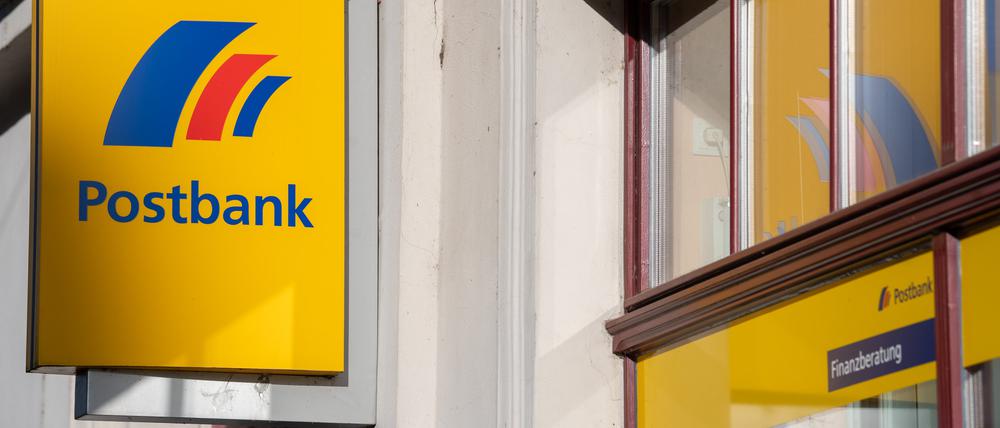 Ein Schild mit dem Logo der Postbank ist an der Fassade einer Bankfiliale angebracht. 