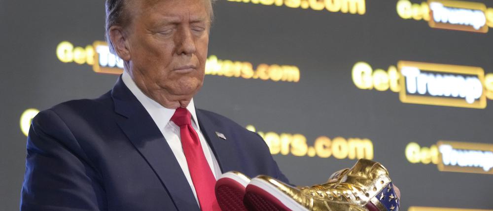 Der republikanische Präsidentschaftskandidat und ehemalige Präsident Donald Trump hält goldene Trump-Sneakers auf der Sneaker Con Philadelphia, einer Veranstaltung für Sneakersammler, in Händen. 