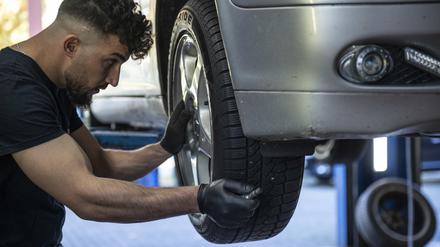 Ein Mechaniker montiert einen Autoreifen an einem Auto in einer Kfz-Werkstatt in Berlin.