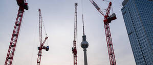 Der Berliner Fernsehturm am Alexanderplatz im Bezirk Mitte waehrend der Abenddaemmerung mit Baukraenen auf der Baustelle des Covivio-Hochhaus.