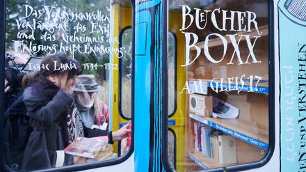 Personen stellen Bücher in die neue „·Bücherbox“ am S-Bahnhof Grunewald.
