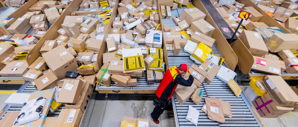 Ein Paketzusteller sortiert und räumt in einer Zustellbasis von Deutsche Post DHL Pakete in ein Zustellfahrzeug.