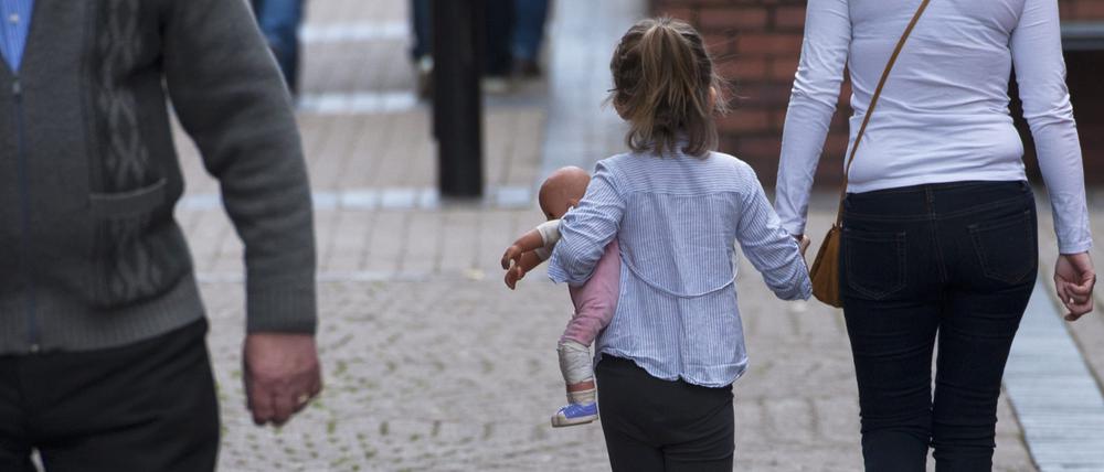 Ein Mädchen mit einer Puppe im Arm geht an der Hand einer Frau durch die Stadt Rotherham.