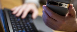 Ein Mann sitzt am Laptop und hält ein Smartphone mit in der Hand. (Symbolbild)