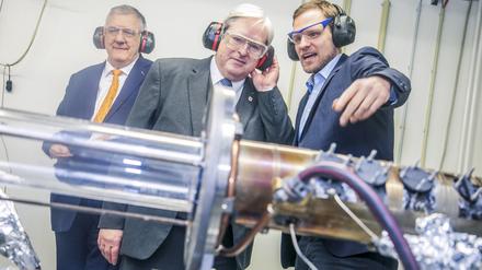 Brandenburgs Wirtschaftsminister Jörg Steinbach (Mitte) lässt sich an der TU Berlin von Tom Tanneberger (r.) zeigen, wie sich Wasserstoff am saubersten und effizientesten verbrennen lässt.