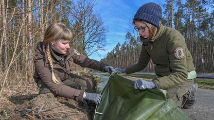 02.03.2022, Brandenburg, Buckow: Henriette Brune (l) und Nora Farnbacher, beide Rangerinnen beim Bundesverband Naturwacht e.V., sind in der Märkischen Schweiz mit dem Aufbau eines Krötenzaunes an einer Straße beschäftigt. Jetzt beginnen vor allem die Erdkröten und Moorfrösche mit der Wanderung. In Folge der milden Temperaturen der vergangenen Tage werden diese Tiere langsam wieder aktiv. Sobald die Nachttemperaturen nicht mehr unter sechs Grad absinken, treten die Kröten, Unken, Molche, Salamander und Frösche ihre Frühjahrswanderung zu den angestammten Laichgewässern an. (zu dpa: «Dramatischer Rückgang von Kröte, Frosch &Co - Saison lässt hoffen») Foto: Patrick Pleul/dpa-Zentralbild/ZB +++ dpa-Bildfunk +++