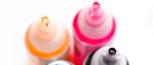 Four open printer bottles with CMYK colour ink. White background. Shallow depth of field