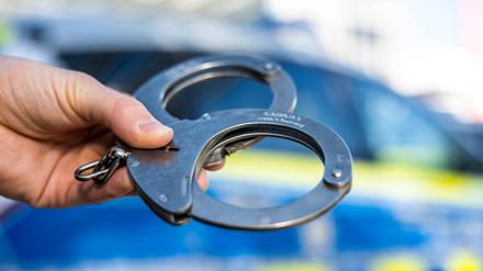 ILLUSTRATION - 28.09.2021, Nordrhein-Westfalen, Gütersloh: Eine Hand hält Handschellen vor einen Streifenwagen der Polizei. (zu dpa: «Verdacht auf Totschlag: 45-Jähriger in U-Haft») (zu dpa: «Mann aus Sachsenheim soll mit Gegenstand auf Opfer eingeschlagen haben») Foto: David Inderlied/dpa +++ dpa-Bildfunk +++