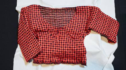 Ein Pullover mit rot-blauem Strickmuster liegt auf einem weißen Tuch.
