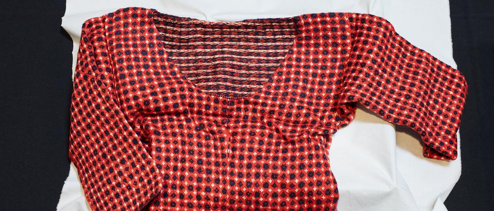 Ein Pullover mit rot-blauem Strickmuster liegt auf einem weißen Tuch.