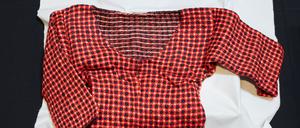 Ein Pullover mit rot-blauem Strickmuster liegt auf einem weißen Tuch.