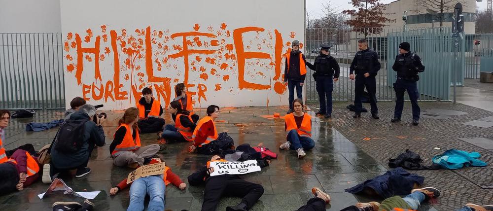 Aktivistinnen und Aktivisten der Letzten Generation sitzen vor einer Wand des Bundeskanzleramts auf der der Schriftzug «Hilfe! Eure Kinder» steht. Teilnehmer der Protestgruppe haben am Samstag die Fassade des Bundeskanzleramts mit orangener Farbe beschmiert.
