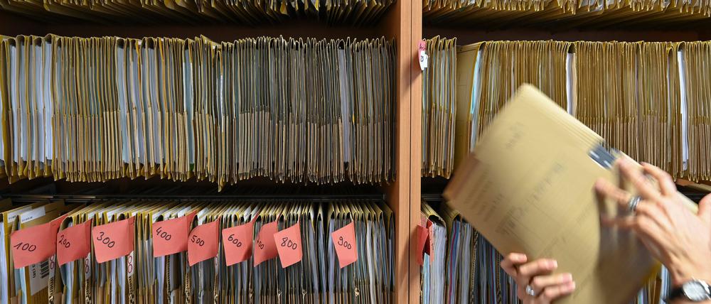 Eine Mitarbeiterin einer Behörde greift an einem Regal nach einer Akte. (Symbolbild)