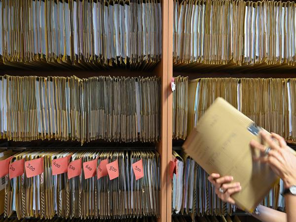 Eine Mitarbeiterin einer Behörde greift an einem Regal nach einer Akte. (Symbolbild)