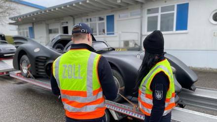 Zwei Abfertigungsbeamte des Zolls stehen bei einer zollrechtlichen Einfuhrkontrolle vor dem „Batmobil“, das auf einem Anhänger steht.