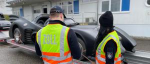 Zwei Abfertigungsbeamte des Zolls stehen bei einer zollrechtlichen Einfuhrkontrolle vor dem „Batmobil“, das auf einem Anhänger steht.