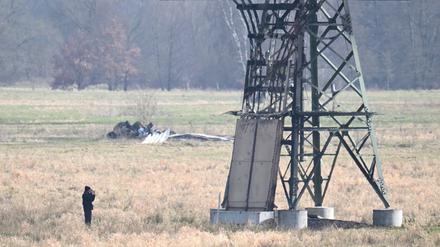 Ein verbrannter Strommast steht auf einem Feld und ein Polizeifotograf dokumentiert die Spuren. In der Tesla-Autofabrik in Grünheide steht die Produktion wegen des dadurch verursachten Stromausfalls still. 