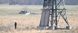 Ein verbrannter Strommast steht auf einem Feld und ein Polizeifotograf dokumentiert die Spuren. In der Tesla-Autofabrik in Grünheide steht die Produktion wegen des dadurch verursachten Stromausfalls still.