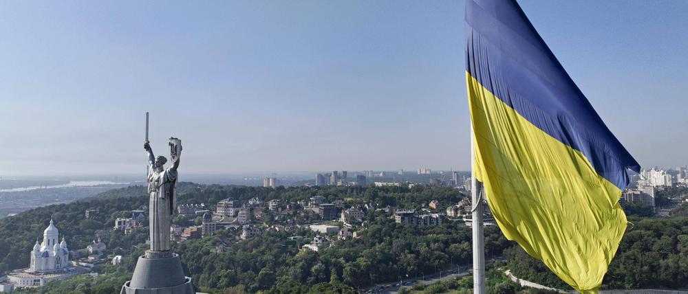Das Mutterlandsdenkmal in Kiew aus der Luft. Im Vordergrund eine ukrainische Fahne.