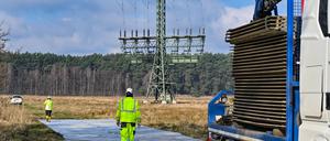 06.03.2024, Brandenburg, Grünheide: Arbeiter errichten eine provisorische Baustraße zu einem Strommast mit Brandspuren auf einem Feld nahe der Tesla-Autofabrik.