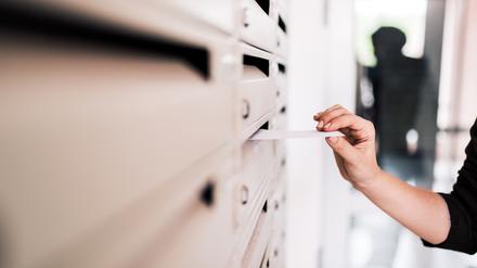 Female person putting letter in metal mailbox, close-up.