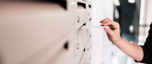 Female person putting letter in metal mailbox, close-up.