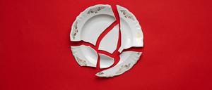 Zerbrochener Teller auf rotem Hintergrund als Symbol für häusliche Gewalt.