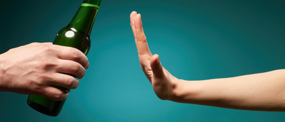 Eine grüne Bierflasche trifft auf eine ablehnende Hand.