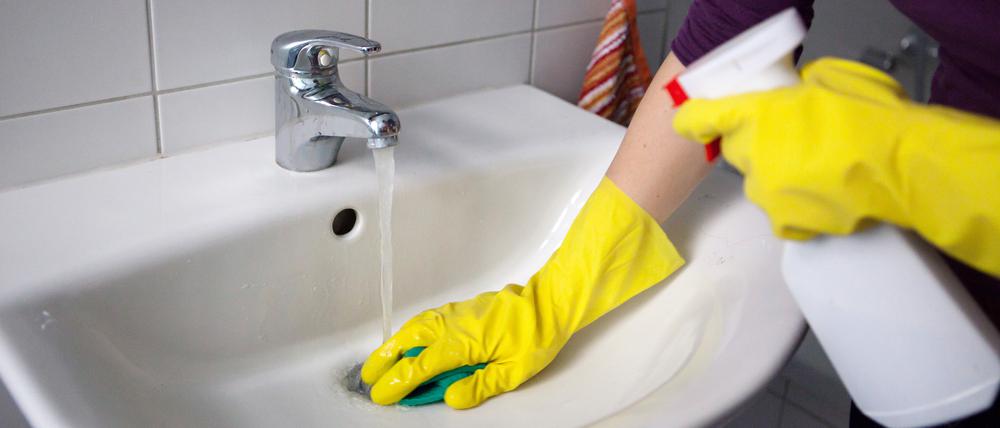 Eine Haushaltshilfe putzt Waschbecken.