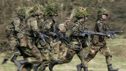 Mit Blattwerk und Gras getarnte Wehrpflichtige von den Panzergrenadieren rennen mit ihren Waffen im Rahmen ihrer Grundausbildung bei einer Übung über das freie Gelände der Knüll Kaserne in Schwarzenborn. (Archivbild)