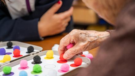 Eine Seniorin spielt ein Gedächtnisspiel, sie hat bunte Spielfiguren in der Hand.