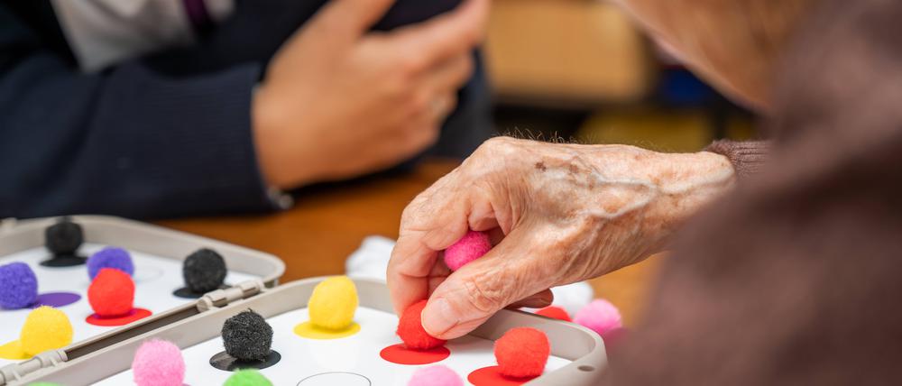 Eine Seniorin spielt ein Gedächtnisspiel, sie hat bunte Spielfiguren in der Hand.